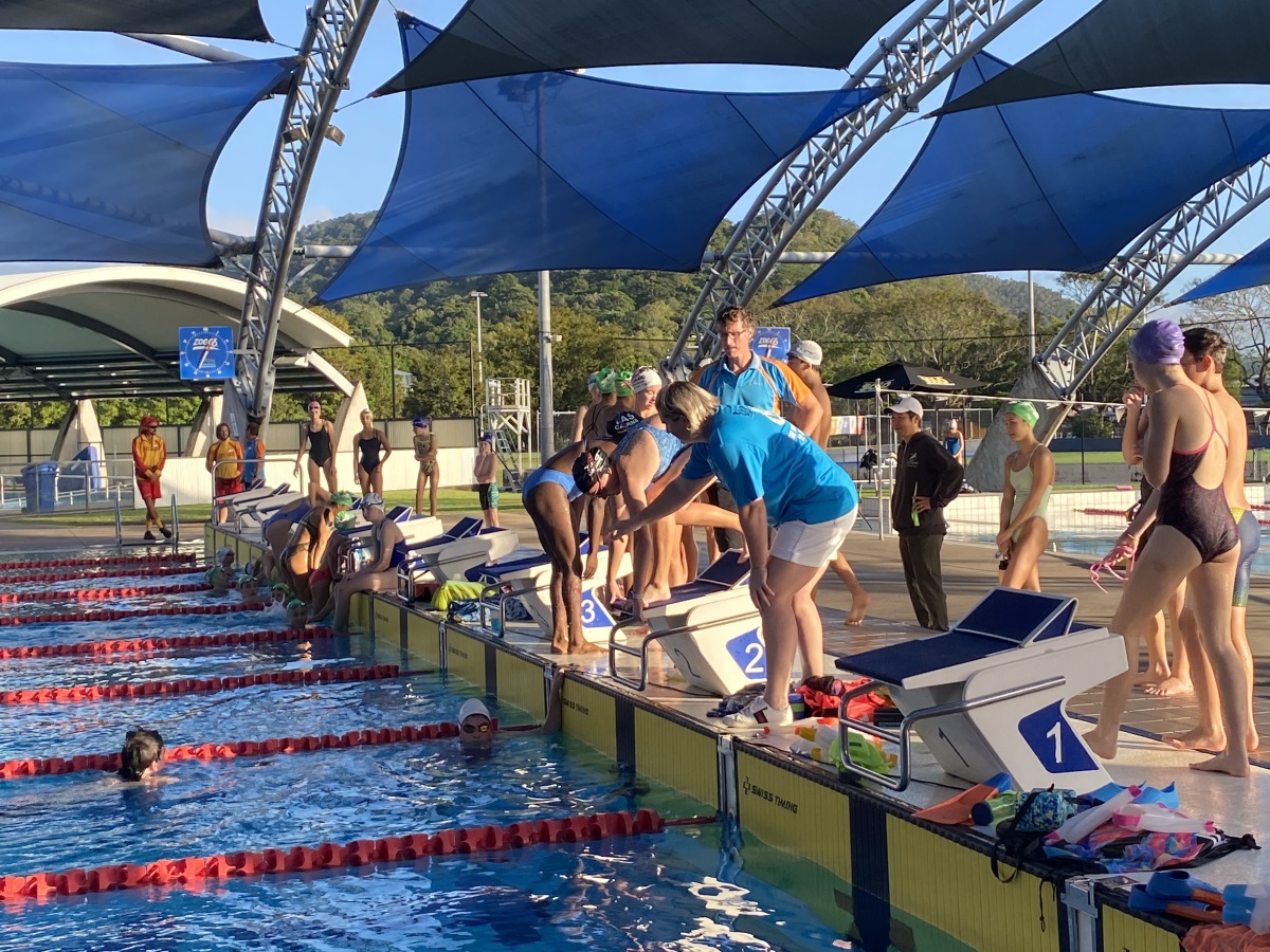 A group of young swimmers in the water, practicing strokes and drills, while others wait their turn