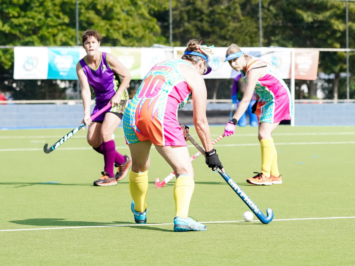 Masters woman hitting hockey ball to teammate